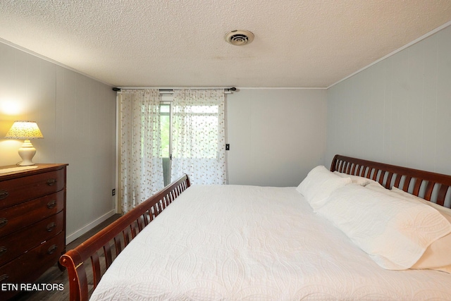bedroom with a textured ceiling, visible vents, ornamental molding, and wood finished floors