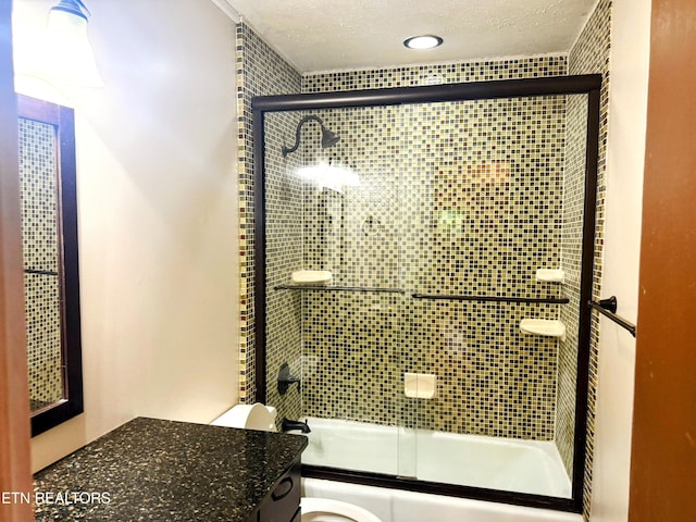 bathroom with vanity, a textured ceiling, enclosed tub / shower combo, and toilet