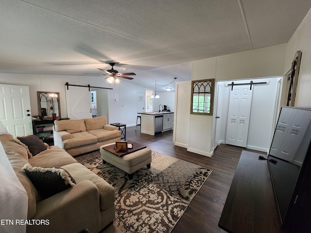 living room featuring a barn door, a textured ceiling, a ceiling fan, baseboards, and dark wood-style floors