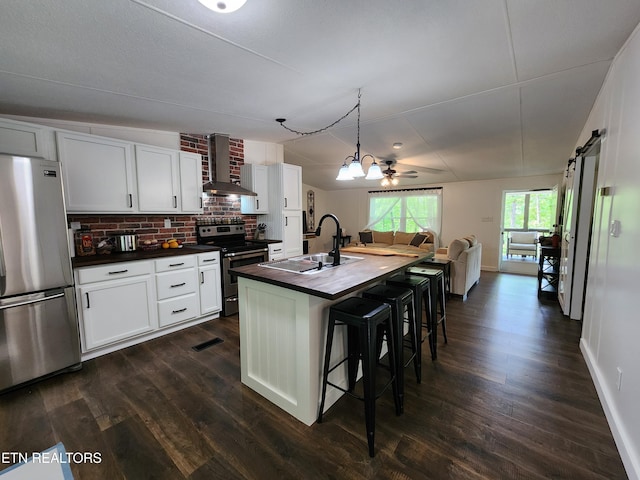 kitchen featuring dark wood-style flooring, a sink, wall chimney exhaust hood, stainless steel appliances, and open floor plan