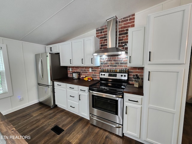 kitchen with wooden counters, wall chimney exhaust hood, stainless steel appliances, backsplash, and vaulted ceiling