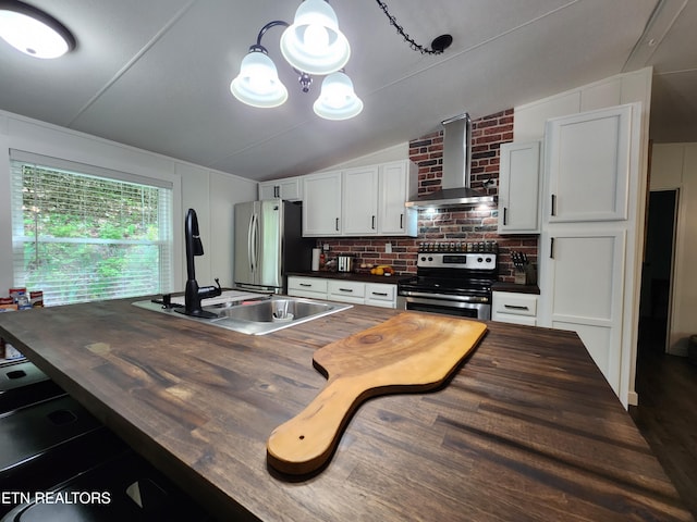 kitchen with butcher block countertops, appliances with stainless steel finishes, a sink, and wall chimney exhaust hood