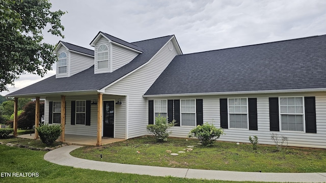 cape cod home with covered porch, a shingled roof, and a front lawn