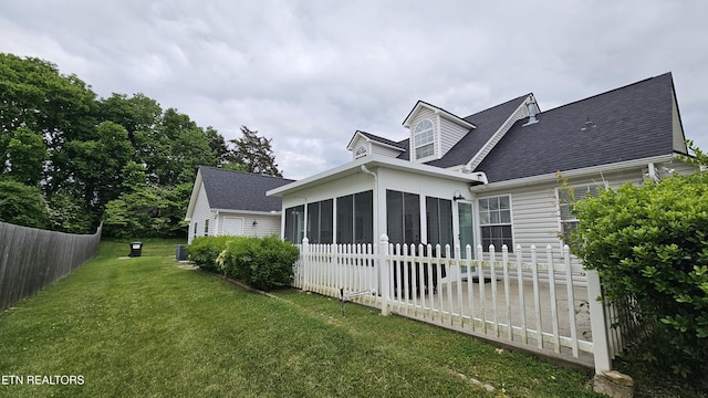 rear view of house with a sunroom, a shingled roof, fence, and a lawn