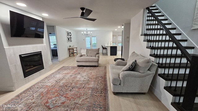 living room featuring recessed lighting, a tiled fireplace, ceiling fan with notable chandelier, stairs, and wood finished floors