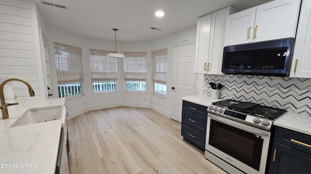 kitchen with a sink, stainless steel gas stove, visible vents, decorative backsplash, and light stone countertops