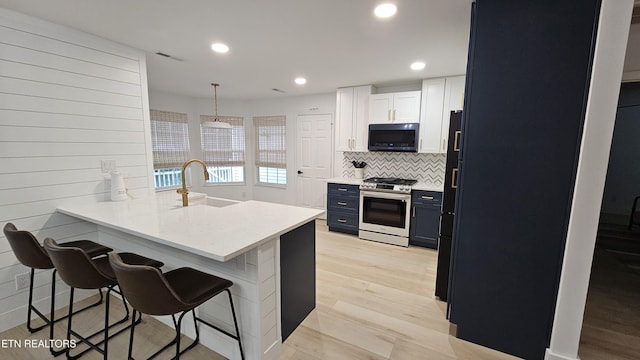 kitchen with a breakfast bar, a sink, a peninsula, blue cabinetry, and stainless steel range with gas stovetop