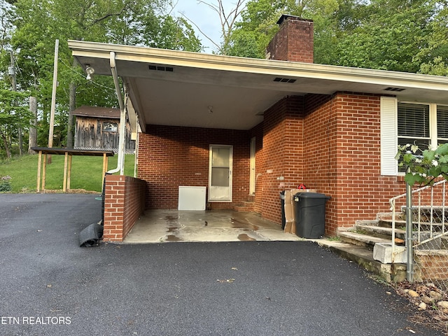 view of front of property with brick siding, an attached carport, driveway, and a chimney