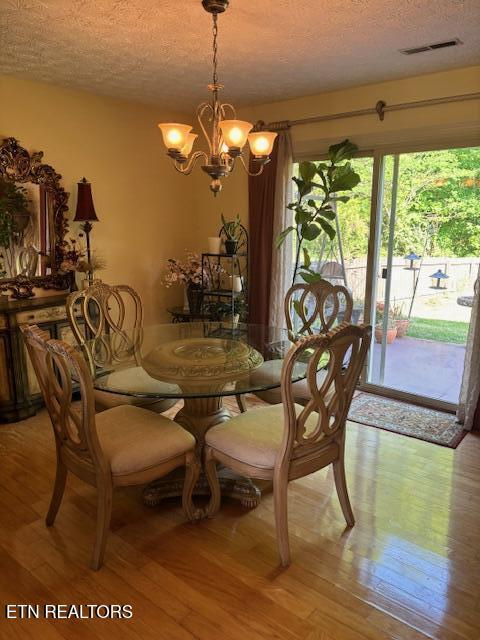 dining room with light wood-type flooring, a textured ceiling, a chandelier, and visible vents