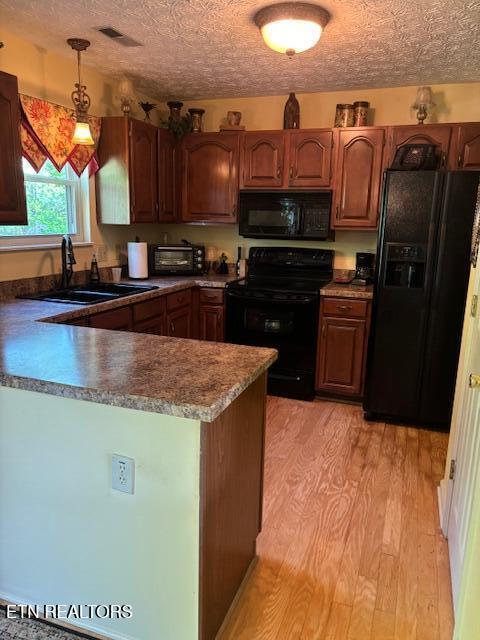 kitchen with visible vents, a sink, black appliances, a peninsula, and light wood-style flooring