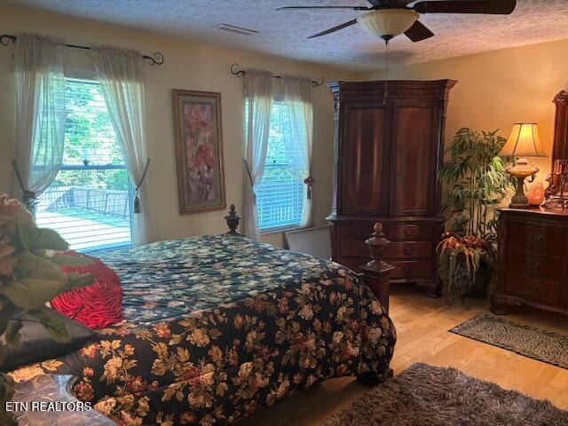 bedroom with light wood-type flooring, a textured ceiling, ceiling fan, and visible vents