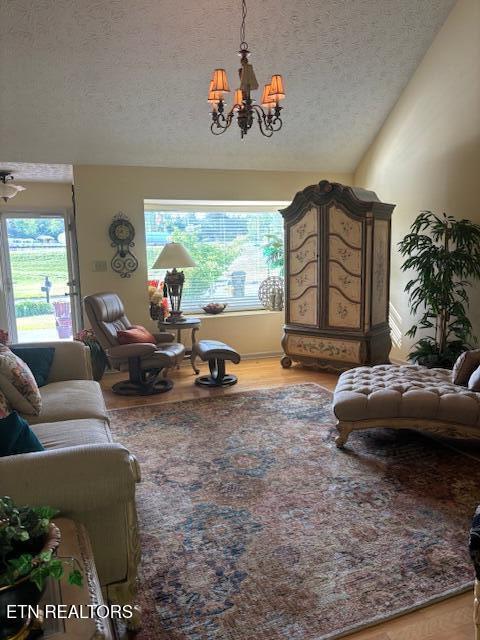 living room featuring wood finished floors, vaulted ceiling, a textured ceiling, and a notable chandelier