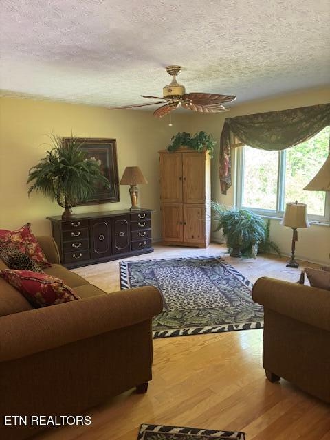 living area featuring light wood-style flooring, a textured ceiling, and ceiling fan