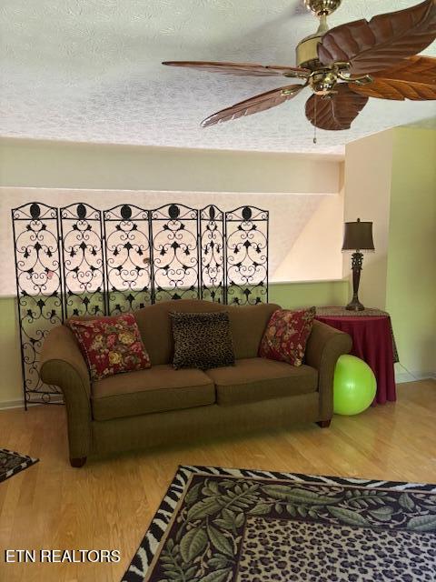 living room with a textured ceiling, ceiling fan, and wood finished floors