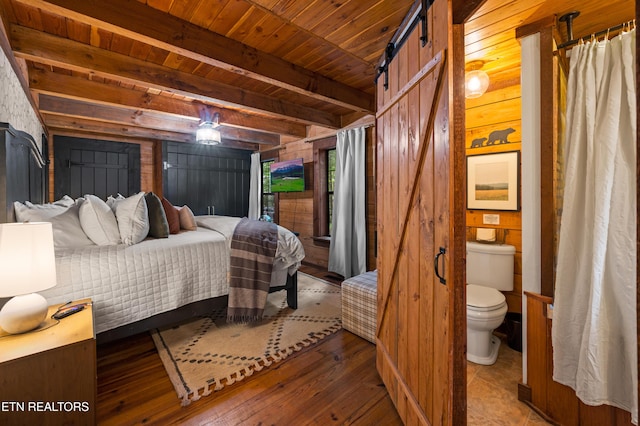 bedroom featuring a barn door, wooden ceiling, wooden walls, hardwood / wood-style floors, and beam ceiling