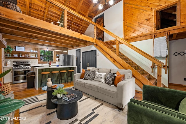 living room featuring light wood-style floors, beam ceiling, wooden ceiling, and stairs