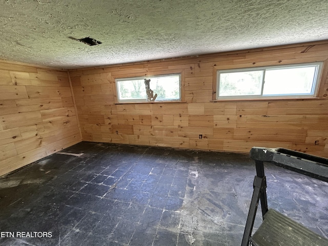 spare room featuring a textured ceiling, wooden walls, and a wealth of natural light