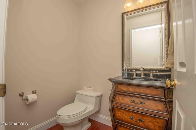 half bathroom with baseboards, wood finished floors, toilet, and vanity