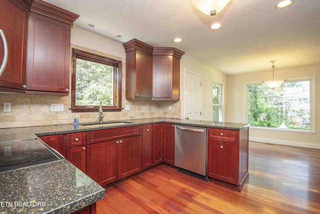 kitchen featuring wood finished floors, dishwasher, a sink, a peninsula, and reddish brown cabinets