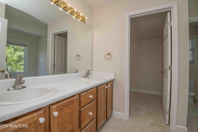 full bathroom featuring double vanity, a sink, baseboards, and toilet