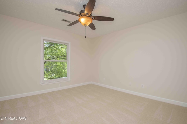 spare room featuring visible vents, light carpet, baseboards, ceiling fan, and a textured ceiling
