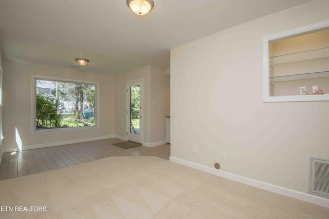 carpeted spare room featuring a healthy amount of sunlight, baseboards, tile patterned flooring, and visible vents