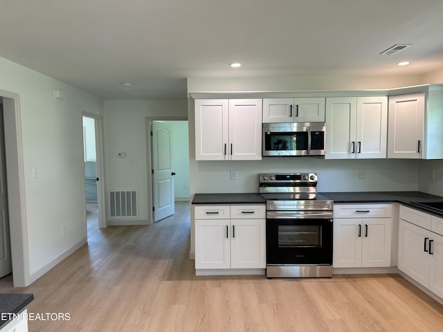 kitchen featuring dark countertops, stainless steel appliances, light wood-style flooring, and visible vents