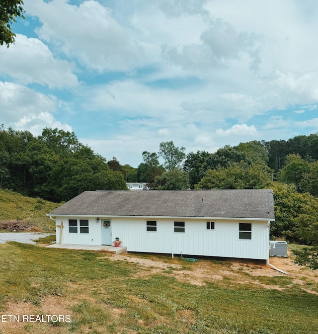 rear view of house with a yard, a shingled roof, and central AC