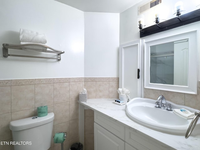 bathroom with tile walls, toilet, wainscoting, visible vents, and vanity