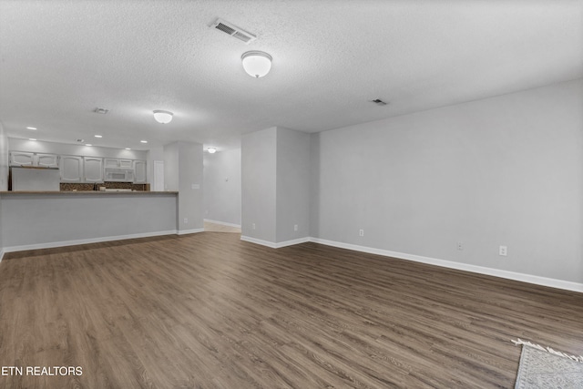 unfurnished living room with dark wood-style flooring, a textured ceiling, visible vents, baseboards, and recessed lighting