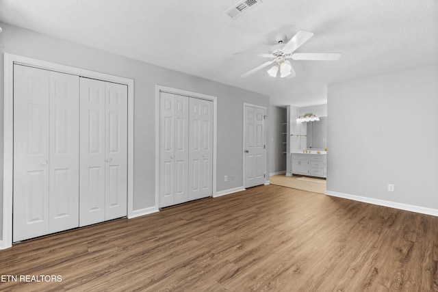 unfurnished bedroom featuring visible vents, baseboards, multiple closets, and wood finished floors