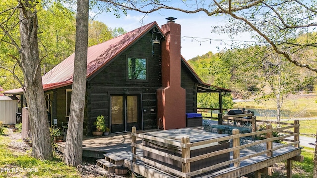 rear view of house featuring a deck, french doors, metal roof, and a chimney