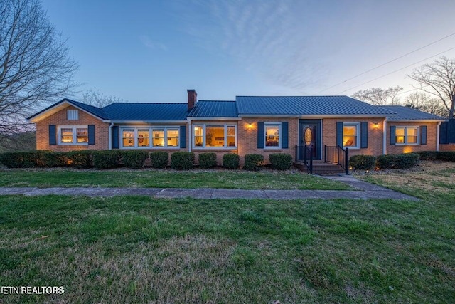 ranch-style house featuring a standing seam roof, a chimney, a yard, and brick siding