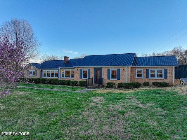 ranch-style home featuring a chimney, a front yard, metal roof, and brick siding