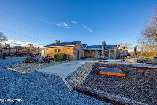 exterior space with fence, a patio, a chimney, brick siding, and metal roof