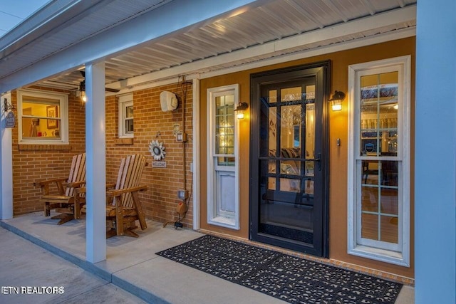 entrance to property featuring a porch and brick siding