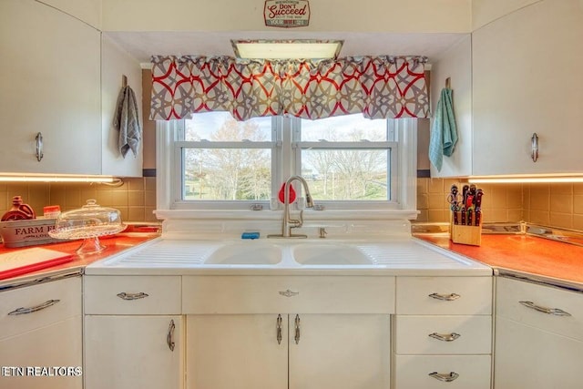 kitchen with a sink, light countertops, decorative backsplash, and white cabinets