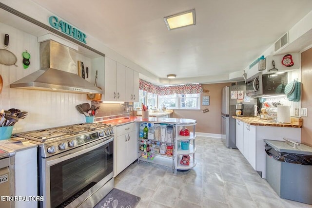 kitchen with wall chimney range hood, white cabinets, stainless steel appliances, a peninsula, and visible vents