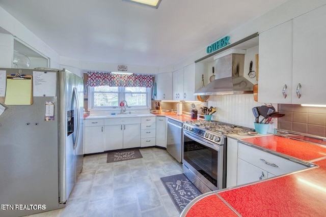 kitchen with backsplash, light countertops, white cabinets, stainless steel appliances, and wall chimney exhaust hood