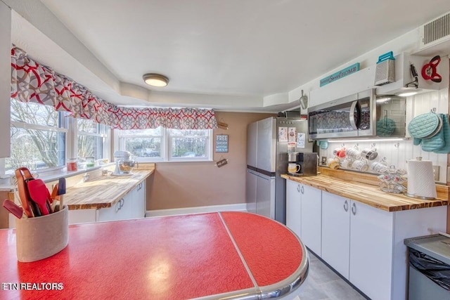 kitchen featuring visible vents, stainless steel appliances, butcher block countertops, and white cabinetry