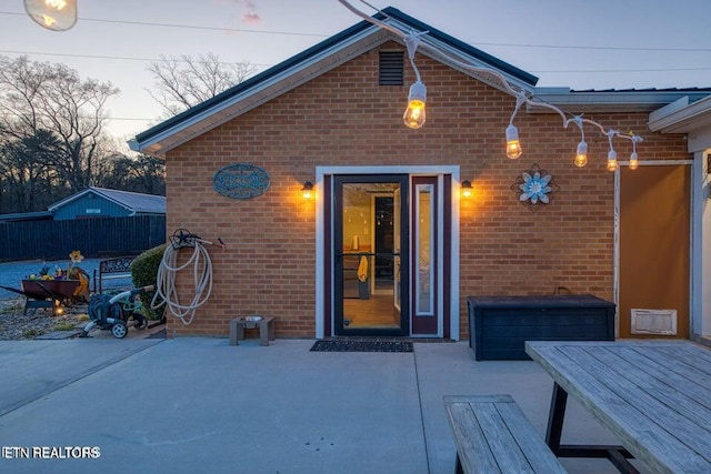 view of exterior entry with brick siding, fence, outdoor dining space, and a patio area