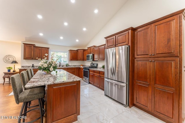 kitchen with a breakfast bar area, a center island, light stone counters, stainless steel appliances, and recessed lighting