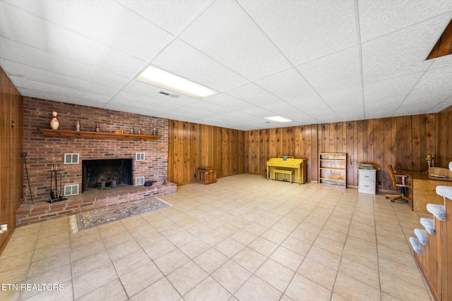 unfurnished living room featuring a brick fireplace, wood walls, a drop ceiling, and visible vents