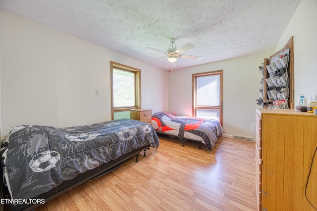 bedroom featuring light wood-style floors, multiple windows, a textured ceiling, and visible vents