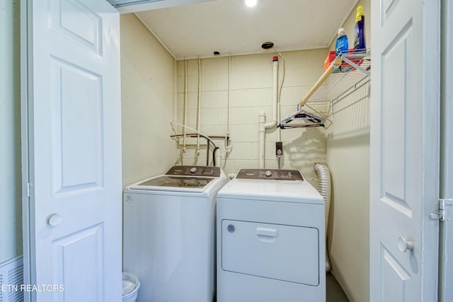 washroom featuring concrete block wall, laundry area, and washing machine and dryer