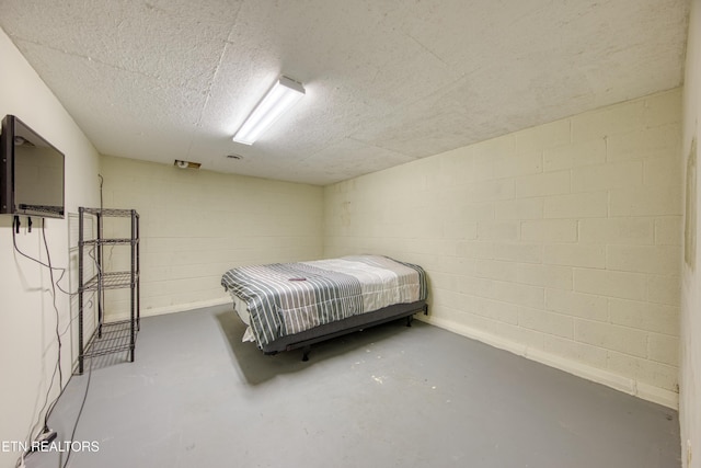 bedroom featuring concrete block wall, a textured ceiling, and finished concrete flooring