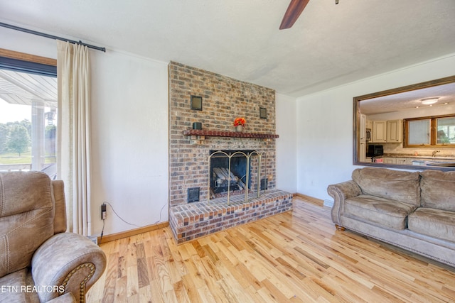 living area with baseboards, a ceiling fan, wood finished floors, and a brick fireplace