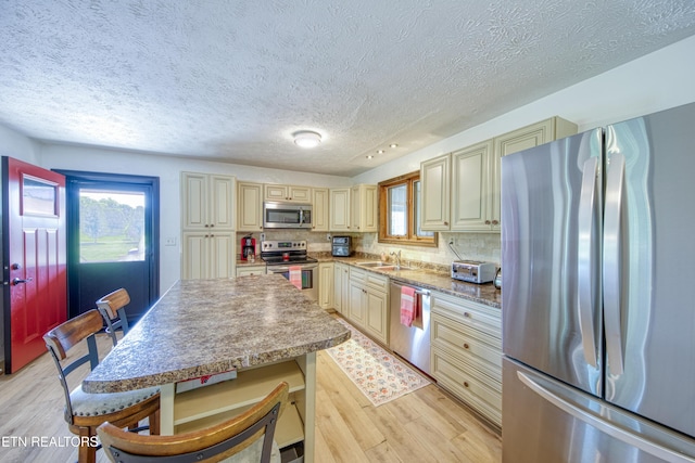 kitchen featuring light wood-style floors, a textured ceiling, cream cabinetry, a sink, and stainless steel appliances