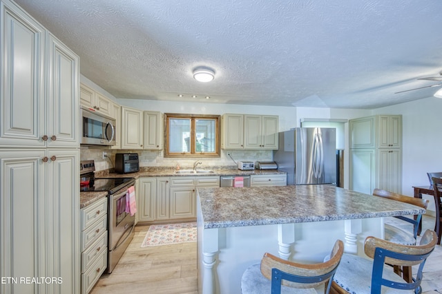 kitchen with a breakfast bar, a center island, a sink, light wood finished floors, and stainless steel appliances