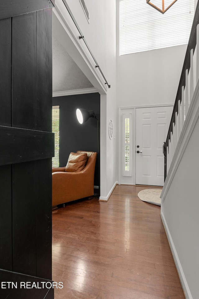 entrance foyer with crown molding, stairs, baseboards, wood finished floors, and a towering ceiling